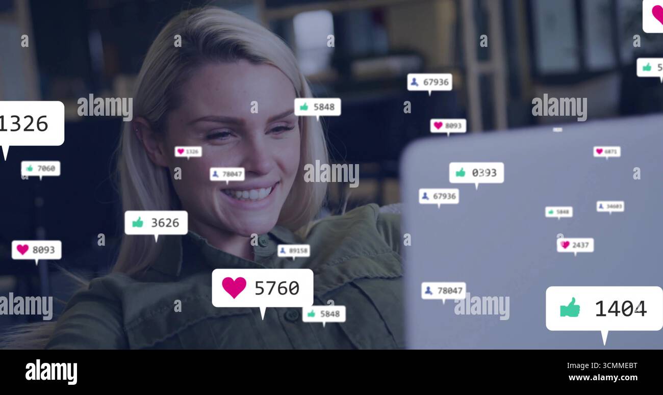 Creatore sorridente in camicia verde oliva che guarda il laptop alla scrivania con icone social fluttuanti e spazio per copiare Foto Stock