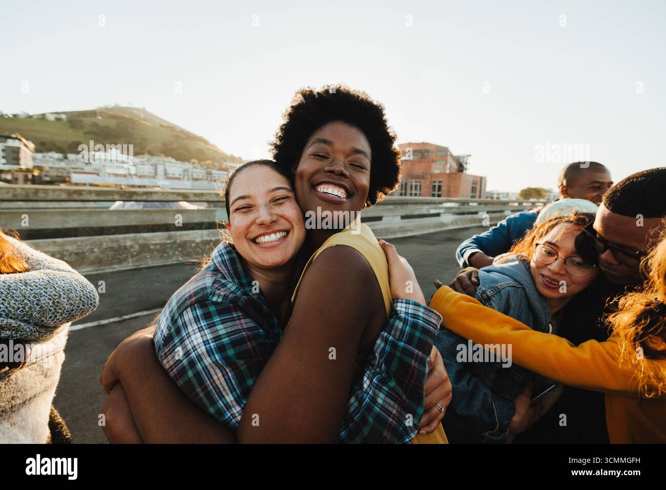 Un gruppo allegro e variegato di persone condivide un abbraccio energico all'aperto sotto la luce del sole. L'immagine trasmette cameratismo, gioia e comunità. Perfetto per p Foto Stock