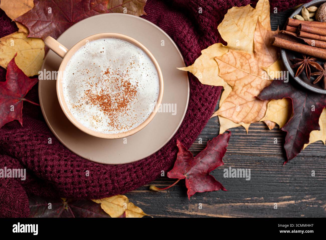 Composizione accogliente autunnale. Tazza di caffè, piano lavorato a maglia, foglie d'acero autunnale rosse e gialle su sfondo in legno, vista dall'alto. Appartamento Hygge stagionale Foto Stock