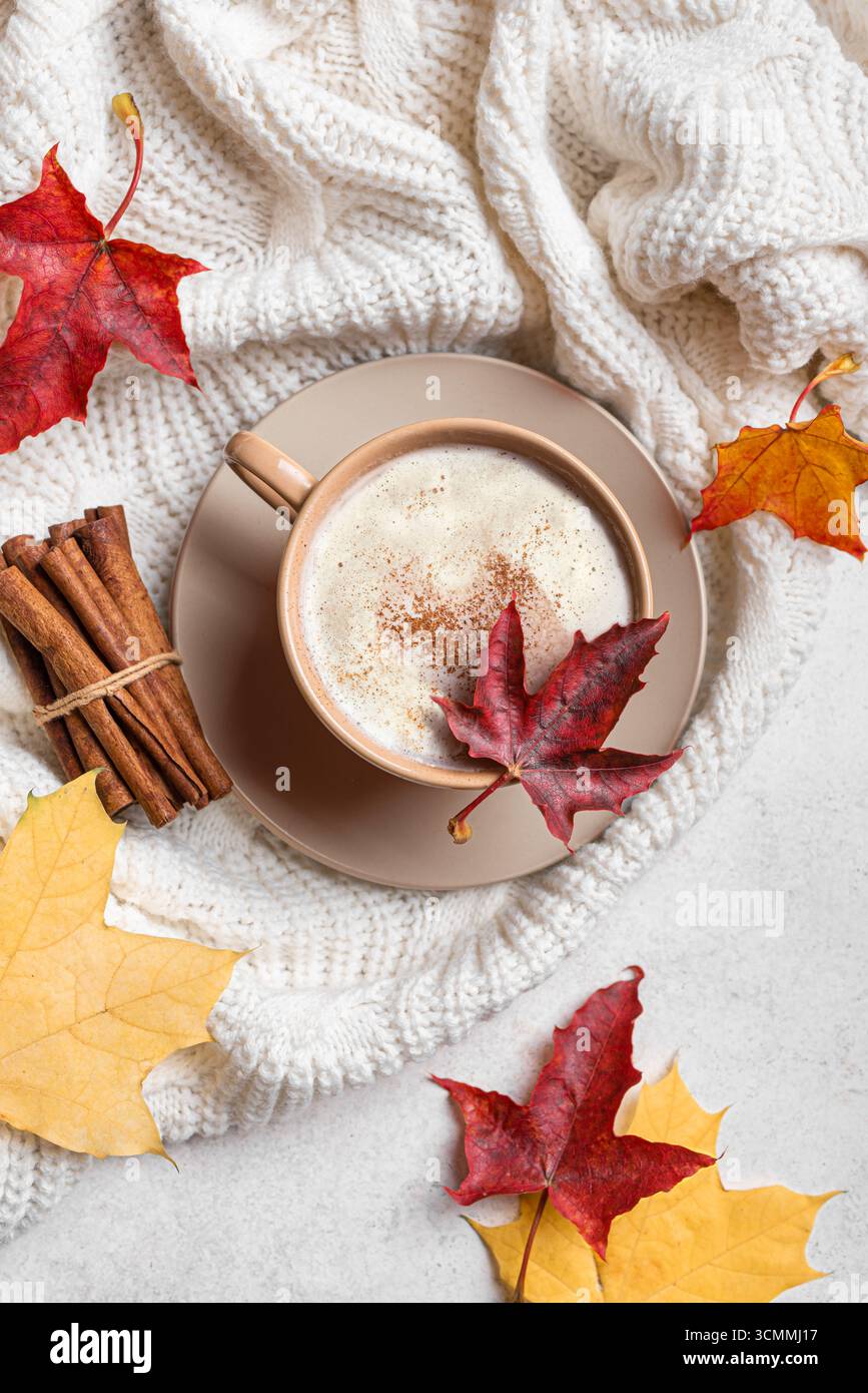 Composizione accogliente autunnale. Tazza di caffè latte con caramello, foglia d'acero sulla parte superiore, plaid lavorato a maglia su sfondo bianco, vista dall'alto. Design piatto Hygge di stagione Foto Stock