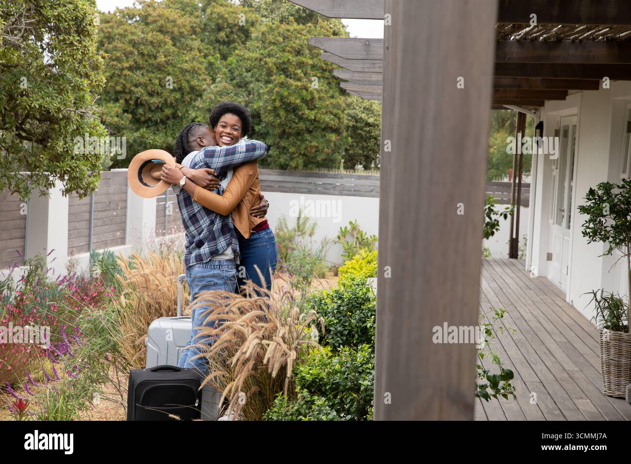 Coppia afroamericana che abbraccia il portico con valigie nere, argento e cappello marrone scuro Foto Stock