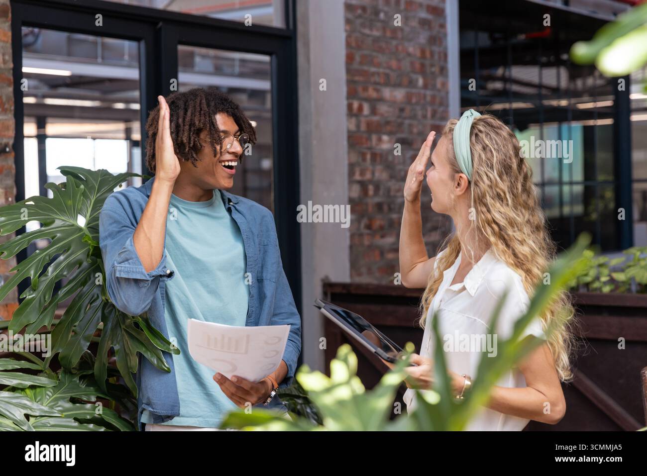 Colleghi eterogenei che lavorano con successo scambiando fogli grafici e tablet in un ufficio moderno con impianti Foto Stock