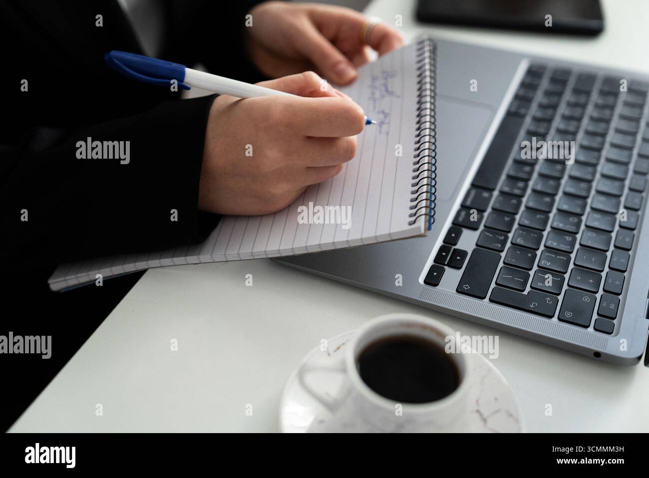 Stretto ritaglio di scrittura accanto a un laptop e a una tazza. Si adatta ai contenuti di pianificazione, studio, copywriting e produttività. Foto Stock