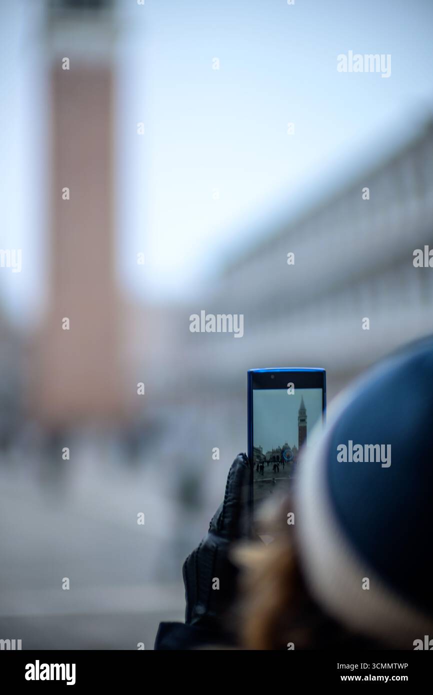 Una persona usa un telefono per inquadrare il Campanile di San Marco nella nebbia invernale di Venezia. La torre è più chiara sullo schermo che nell'atmosfera umida. Foto Stock