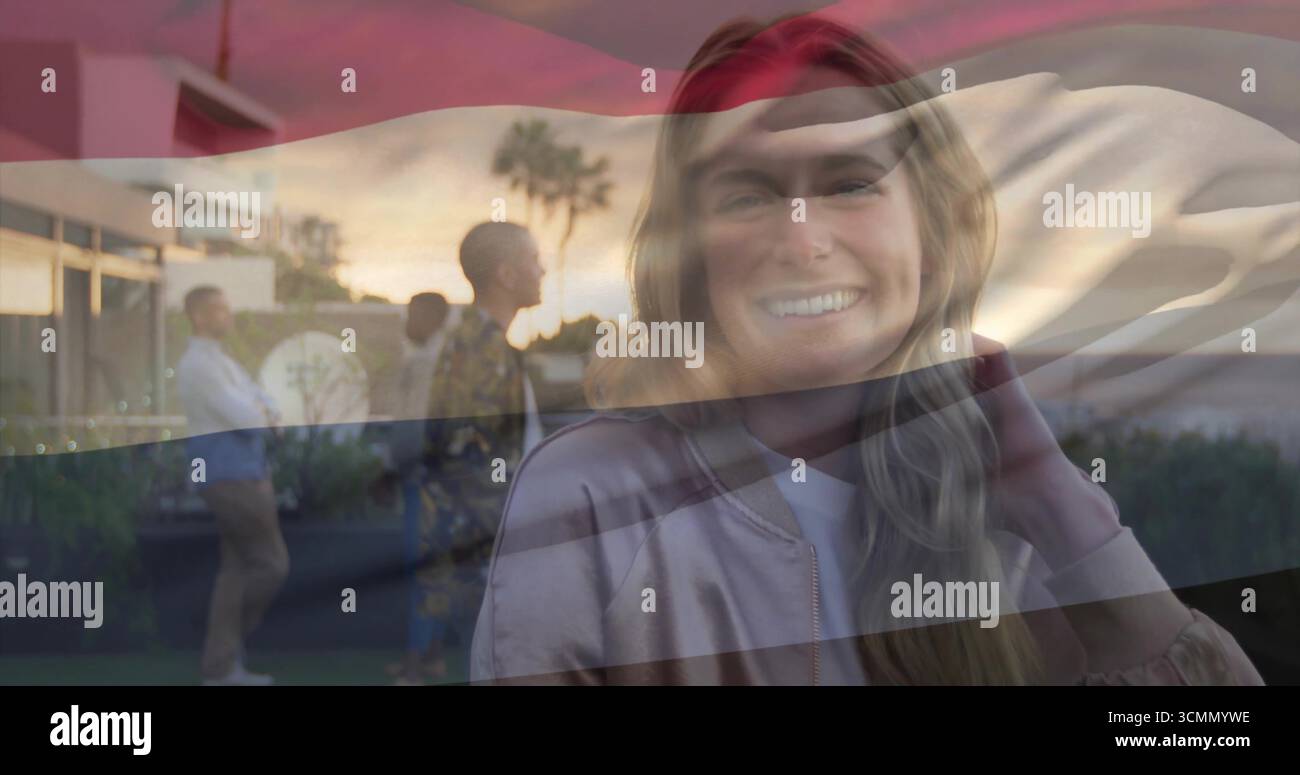 Donna adulta sorridente che indossa un bomber che regola i capelli sulla terrazza al tramonto, con palme Foto Stock
