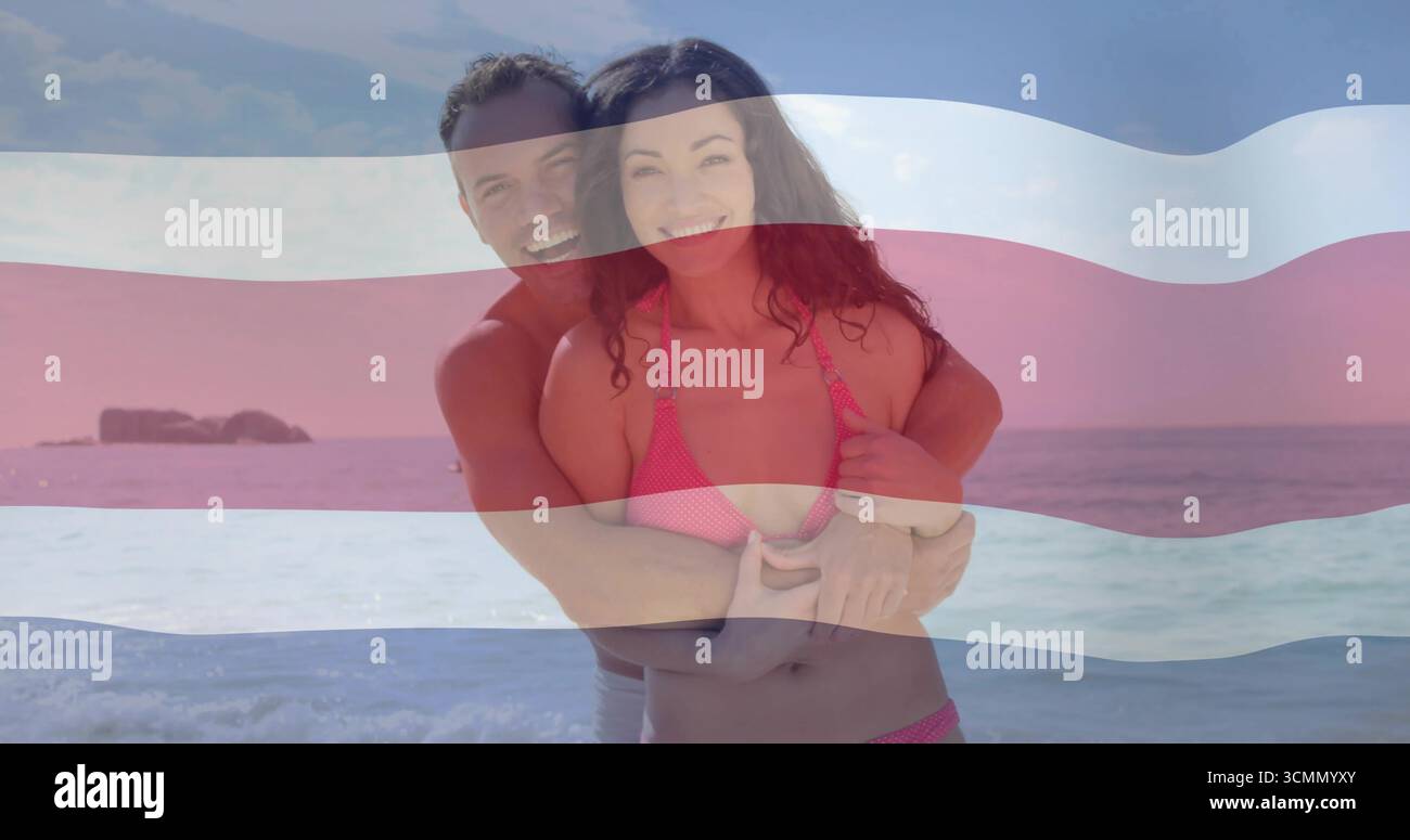 Abbracciando la coppia che indossa bikini rosa e costume da bagno sulla costa dell'oceano, con sovrapposizione a strisce a bandiera Foto Stock