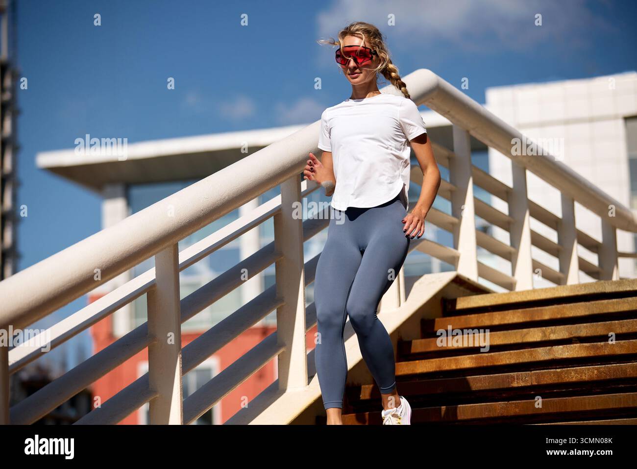 Una giovane donna ama allenarsi al mattino mentre corre all'aperto su una scala indossando abbigliamento sportivo alla moda, rimanendo concentrata ed energizzata. La sua attivita' e' alta Foto Stock