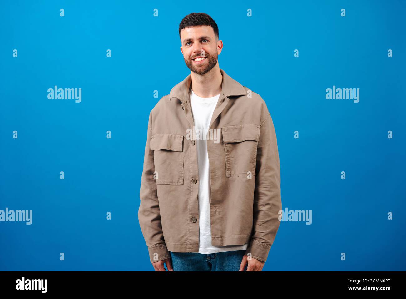 Giovane uomo con barba sorridente in piedi su sfondo blu in un outfit casual Foto Stock