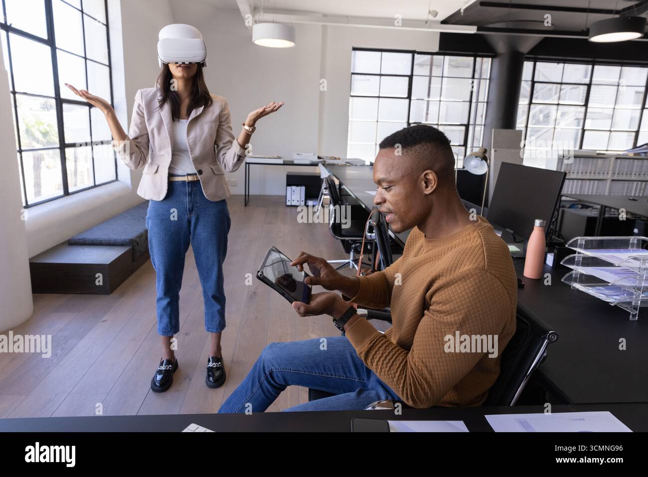 Colleghi diversi che toccano il tablet e indossano il visore vr in un ufficio open space Foto Stock