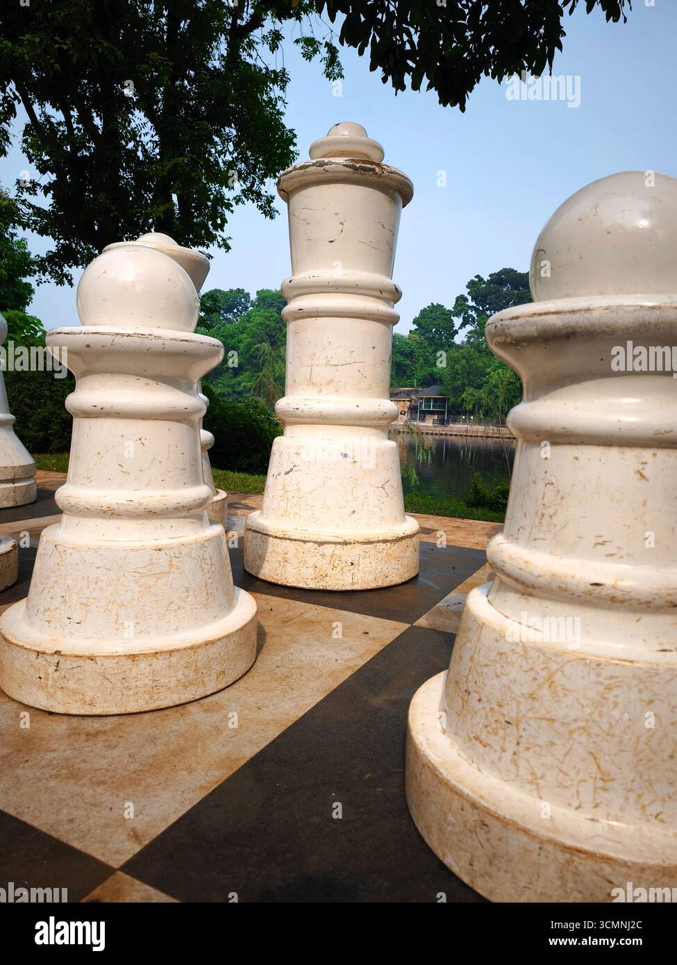Un gigantesco pezzo bianco del re è incorniciato da altri pezzi di scacchi all'aperto posti su una grande scacchiera con sfondo naturale. Foto Stock