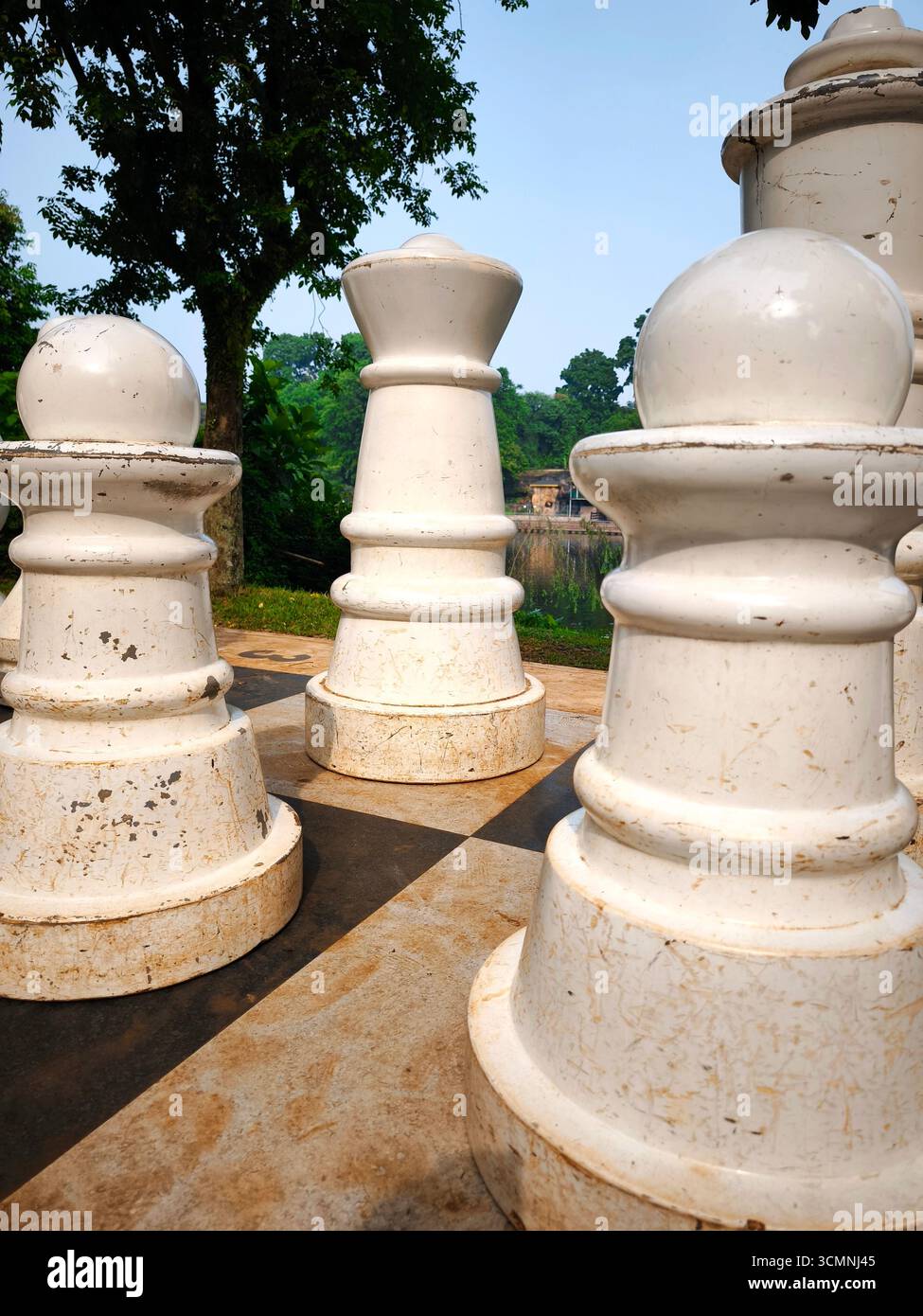 Un pezzo gigante della regina è incorniciato da altri pezzi di scacchi all'aperto posizionati su una grande scacchiera con sfondo naturale. Foto Stock