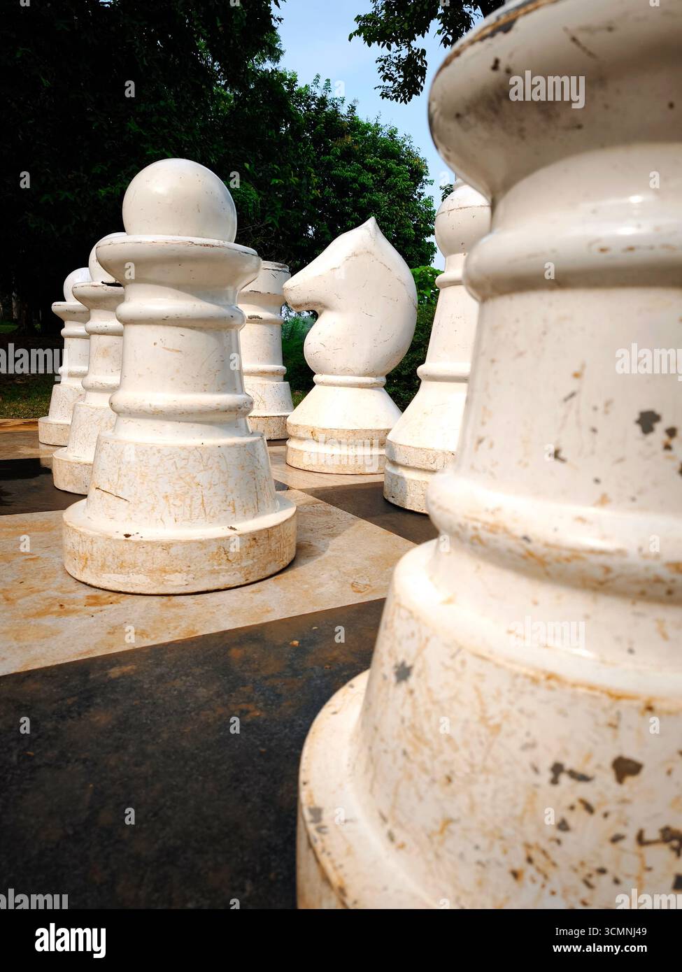Un primo piano di giganteschi pezzi di scacchi all'aperto posizionati su una grande scacchiera a scacchi. I pezzi, compresi pedine e cavalieri, sono realizzati in materiale bianco Foto Stock