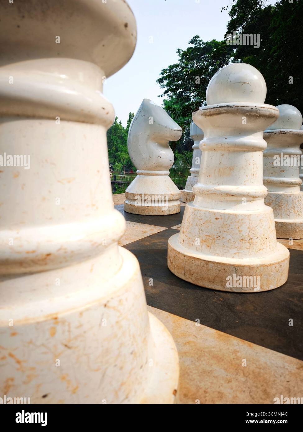 Un gigantesco cavaliere bianco è incorniciato da altri pezzi di scacchi all'aperto posti su una grande scacchiera. Foto Stock
