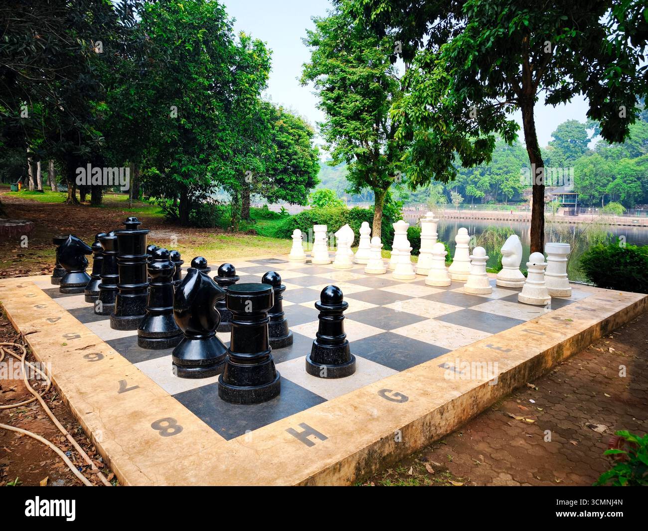Una scacchiera gigantesca all'aperto con grandi scacchi bianchi e neri disposti per il gioco. La tavola è situata in un parco circondato da un'atmosfera naturale Foto Stock