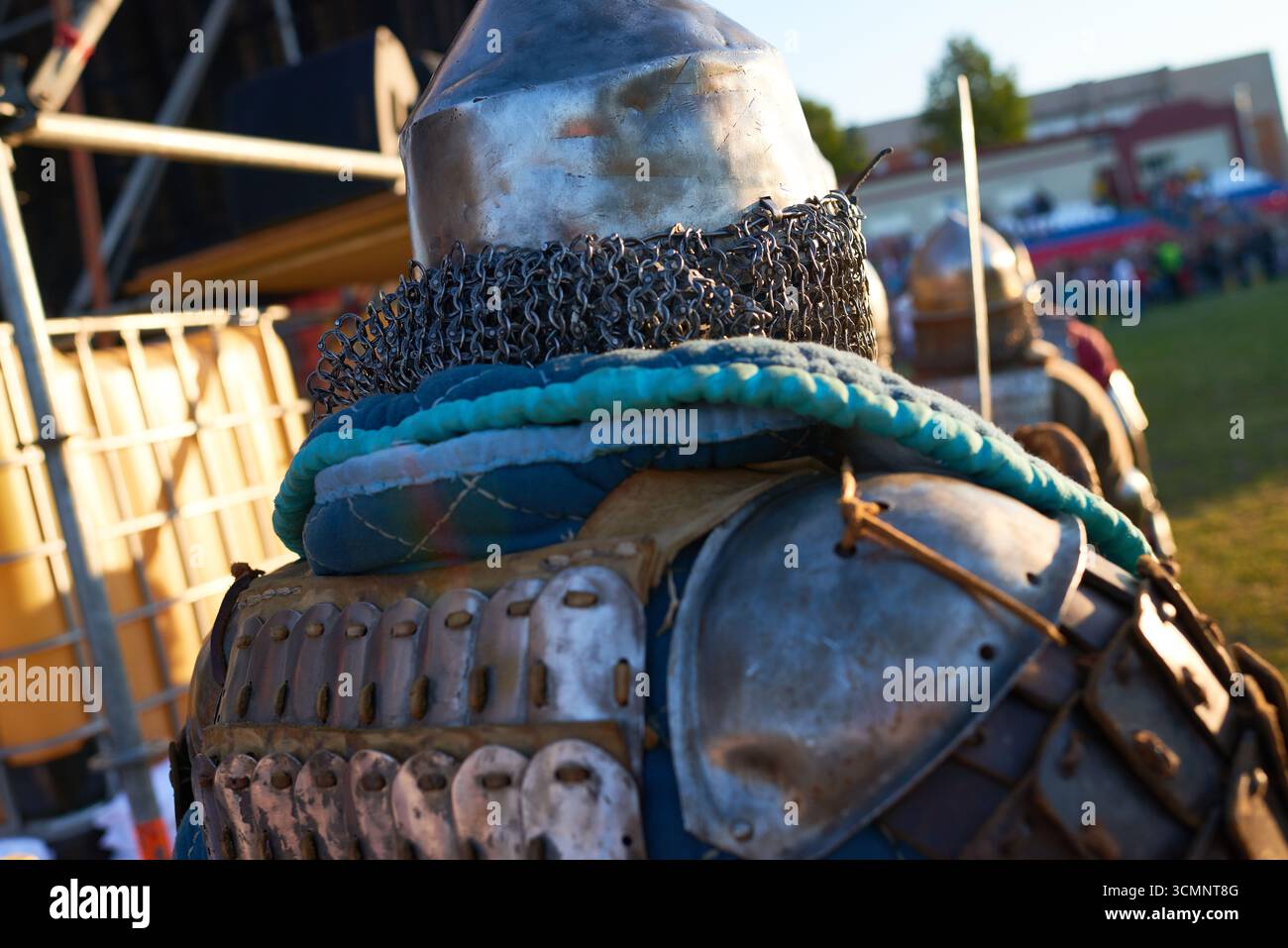 Vista posteriore di un uomo adulto che indossa un'armatura medievale e una chainmail che partecipa a una rievocazione storica all'aperto durante il giorno di sole con altri individui blindati nelle vicinanze Foto Stock