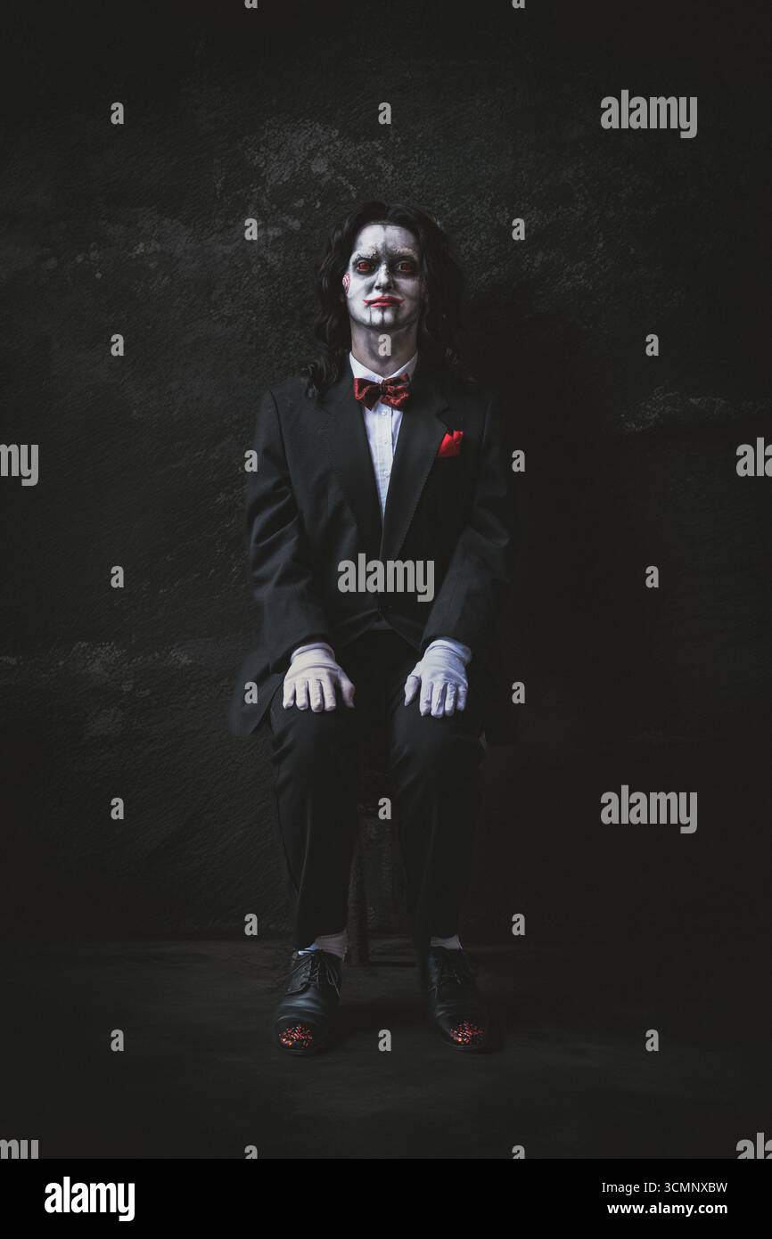 YORK, REGNO UNITO - 31 AGOSTO 2025. Un cosplayer maschile vestito da Billy the Puppet dei film horror visti seduto in una spaventosa stanza buia con spazio per le copie Foto Stock