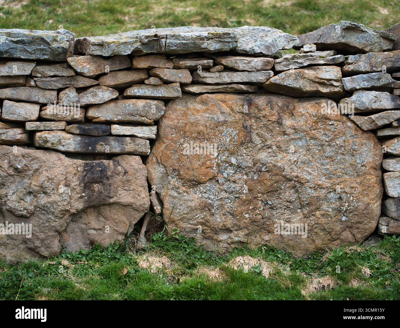 Parete in pietra a secco ruvida e ruvida in un campo - Un'immagine orizzontale full-frame di un muro rustico in pietra a secco con grandi pietre ruvide circondate Foto Stock