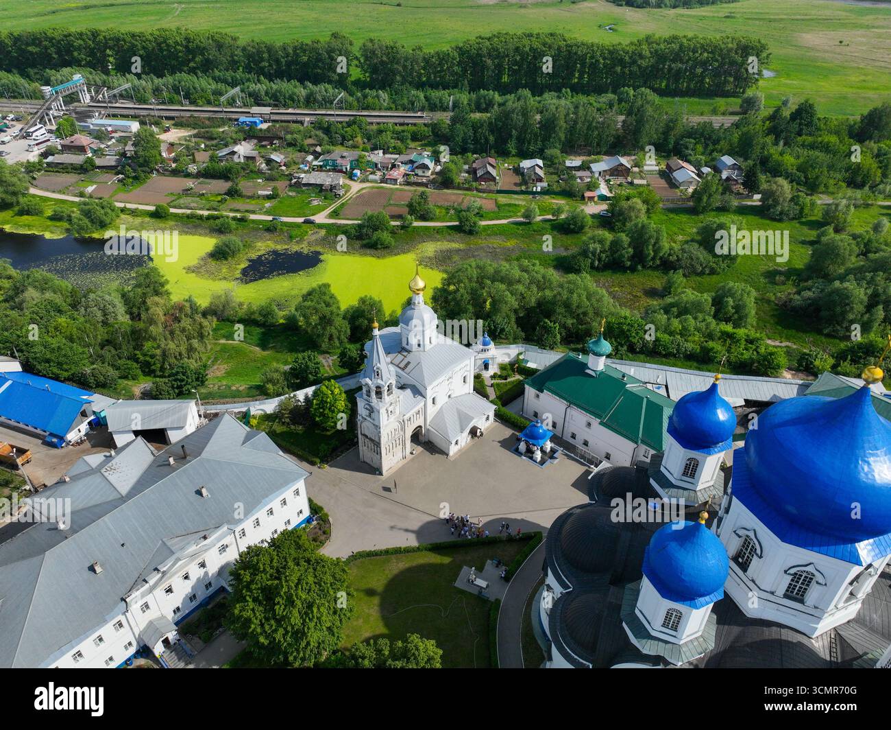 Una vista aerea del complesso del Monastero di Bogolyubovo, che mostra i suoi edifici bianchi e uno stagno con una superficie verde brillante, circondato da campi verdi. Foto Stock