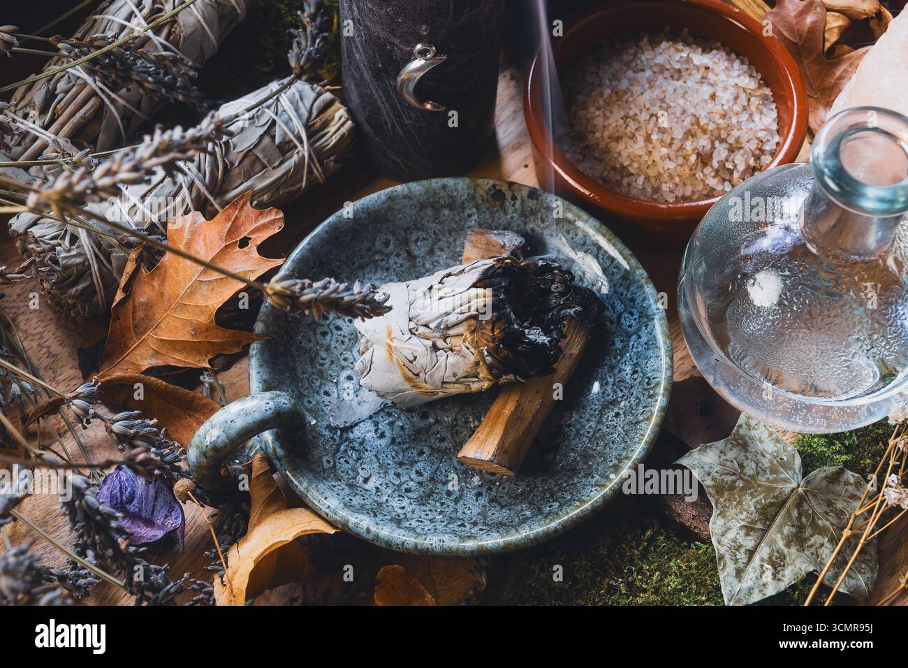 Primo piano di un mistico altare Wiccan con bastoncino macchiato, erbe, sale e strumenti rituali circondati da foglie e cristalli essiccati Foto Stock