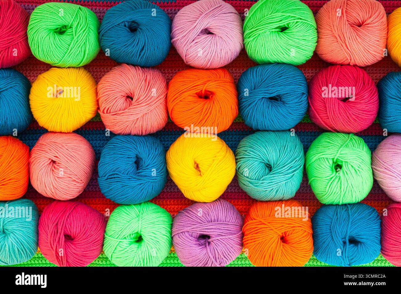Molte sfere di fili multicolore su un tessuto lavorato a maglia, primo piano. Foto Stock