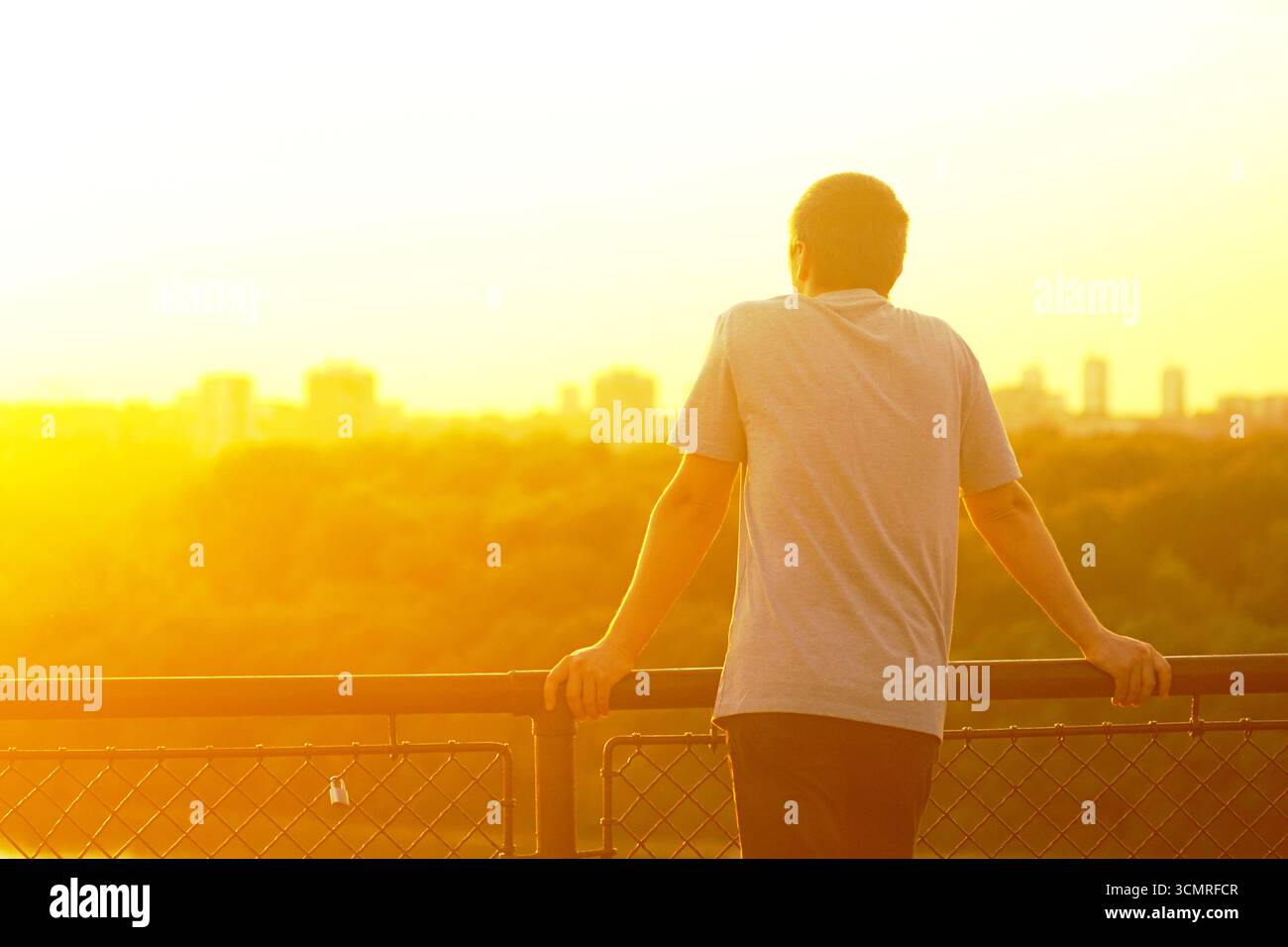 Tramonto dorato su Belgrado dalla fortezza di Kalemegdan. Un uomo si appoggia sulla ringhiera, osservando edifici e natura. Viaggi, armonia urbana, turismo lento Foto Stock