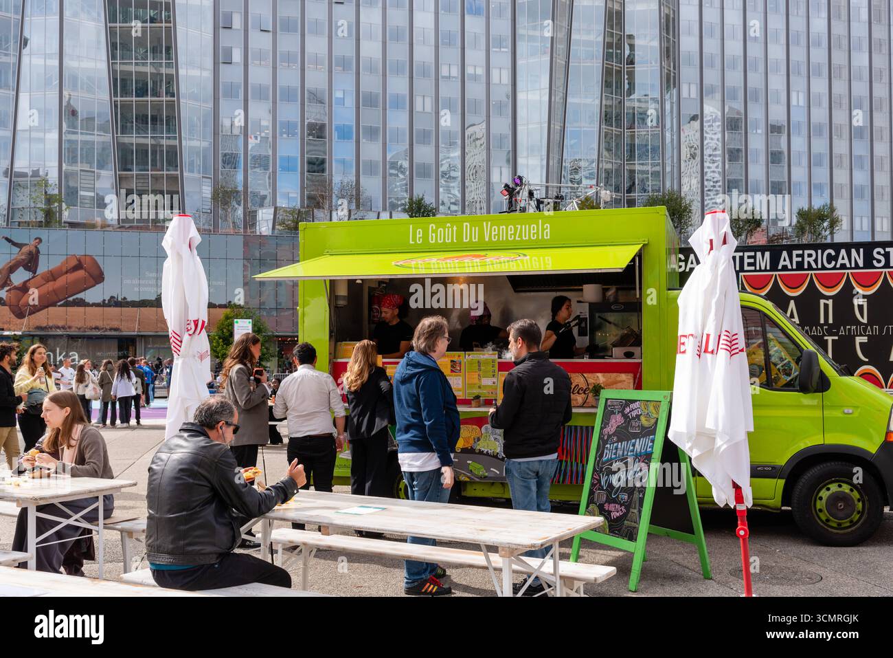 Un camion di cibo verde luminoso che serve cibo venezuelano nel quartiere degli affari di la Défense alla periferia di Parigi. Persone in fila per il cibo da asporto Foto Stock