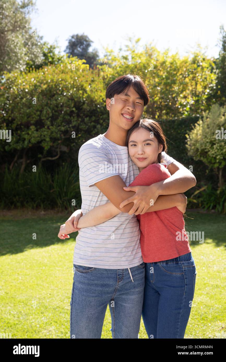 Coppia asiatica che abbraccia e sorride in un giardino privato su un prato verde sotto la luce del sole Foto Stock