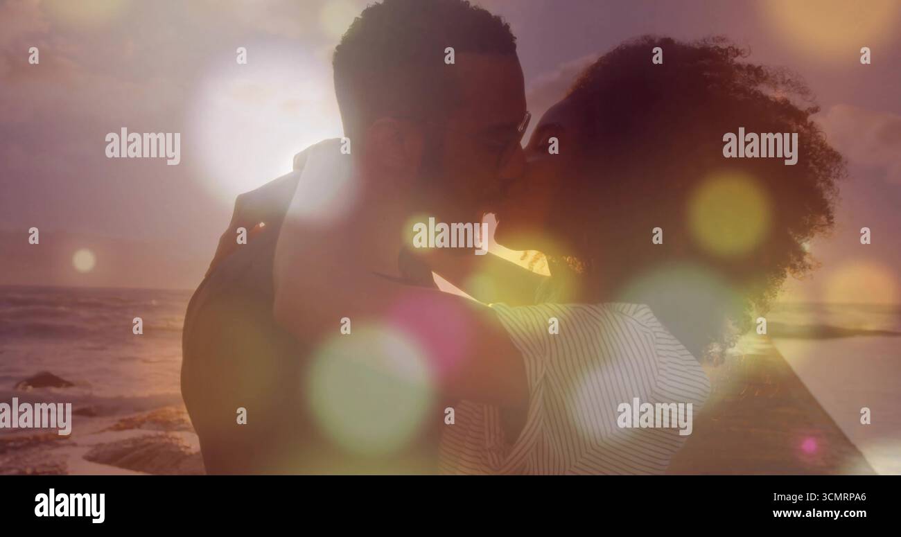 Coppia romantica in piedi che avvolge le braccia e si piega per un bacio sul molo di legno al tramonto e sulle onde dell'oceano Foto Stock