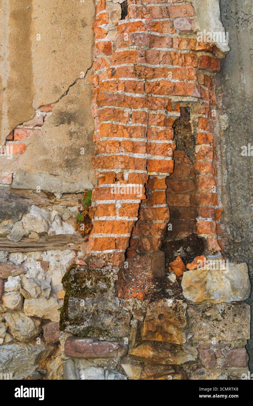 Vista dettagliata di un muro in mattoni e pietra in deterioramento che mostra crepe, erosione e agenti atmosferici, evidenziando il decadimento architettonico rustico e storico Foto Stock