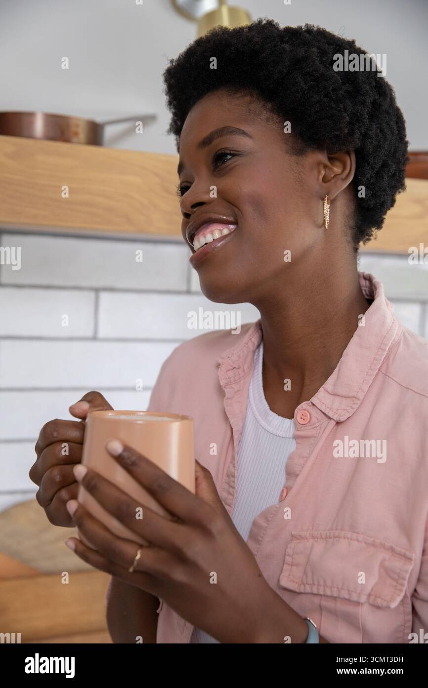 Donna afroamericana di medie dimensioni con tazza da caffè in cucina con teglia in rame Foto Stock