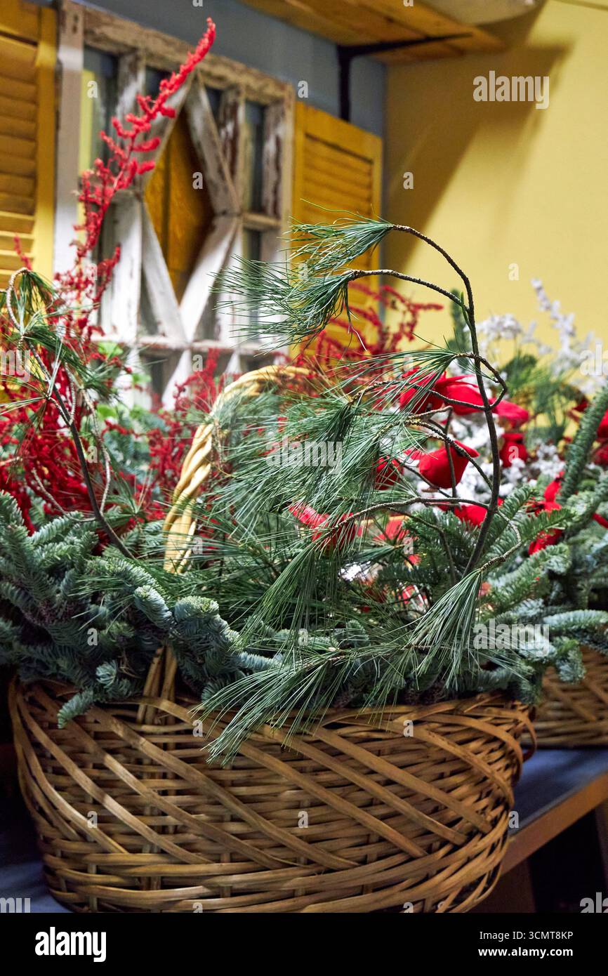 Grande cestino natalizio con rami di pino, cardinali rossi, ornamenti e vegetazione invernale. Una luminosa disposizione floreale natalizia che simboleggia le festività spir Foto Stock