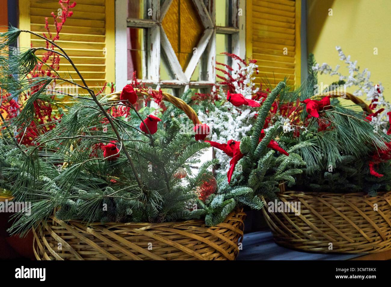 Grande cestino natalizio con rami di pino, cardinali rossi, ornamenti e vegetazione invernale. Una luminosa disposizione floreale natalizia che simboleggia le festività spir Foto Stock