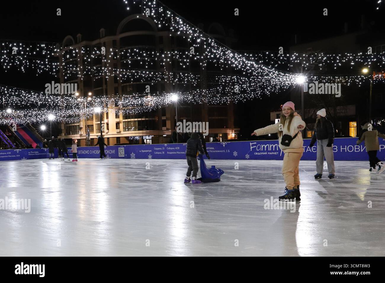 Pista di pattinaggio su ghiaccio all'aperto a Kremenchuk in Ucraina con persone che pattinano sotto le luci festive il 15 gennaio 2025. Atmosfera natalizia e attività stagionali. Foto Stock