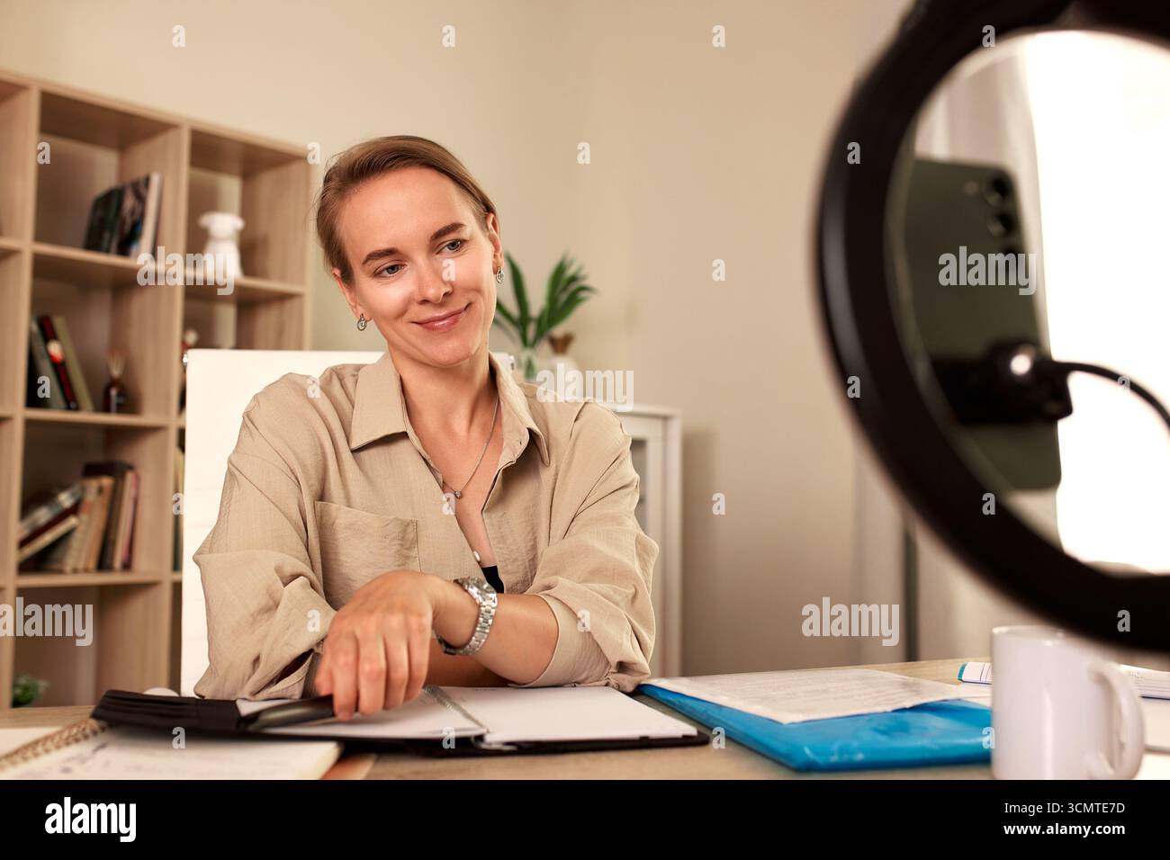 Una donna sicura di sé è impegnata in una videochiamata mentre è seduta alla sua scrivania organizzata in un ufficio ben illuminato. Sembra concentrata e professionale, creando un Foto Stock
