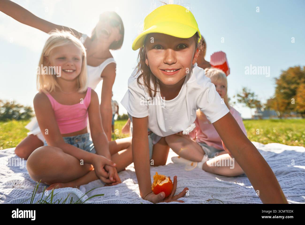 Un gruppo vivace di bambini che trascorrono del tempo insieme in una giornata di sole. Sono seduti su una coperta in un parco, godendosi la compagnia reciproca con sorrisi a Foto Stock