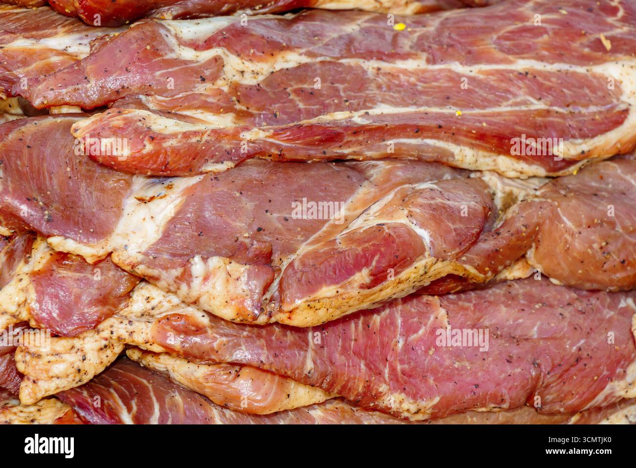 Primo piano di fette di maiale crude marinate con condimento ed erbe aromatiche, impilate come fondo di carne pronto per la cottura alla griglia o la cottura. Foto Stock