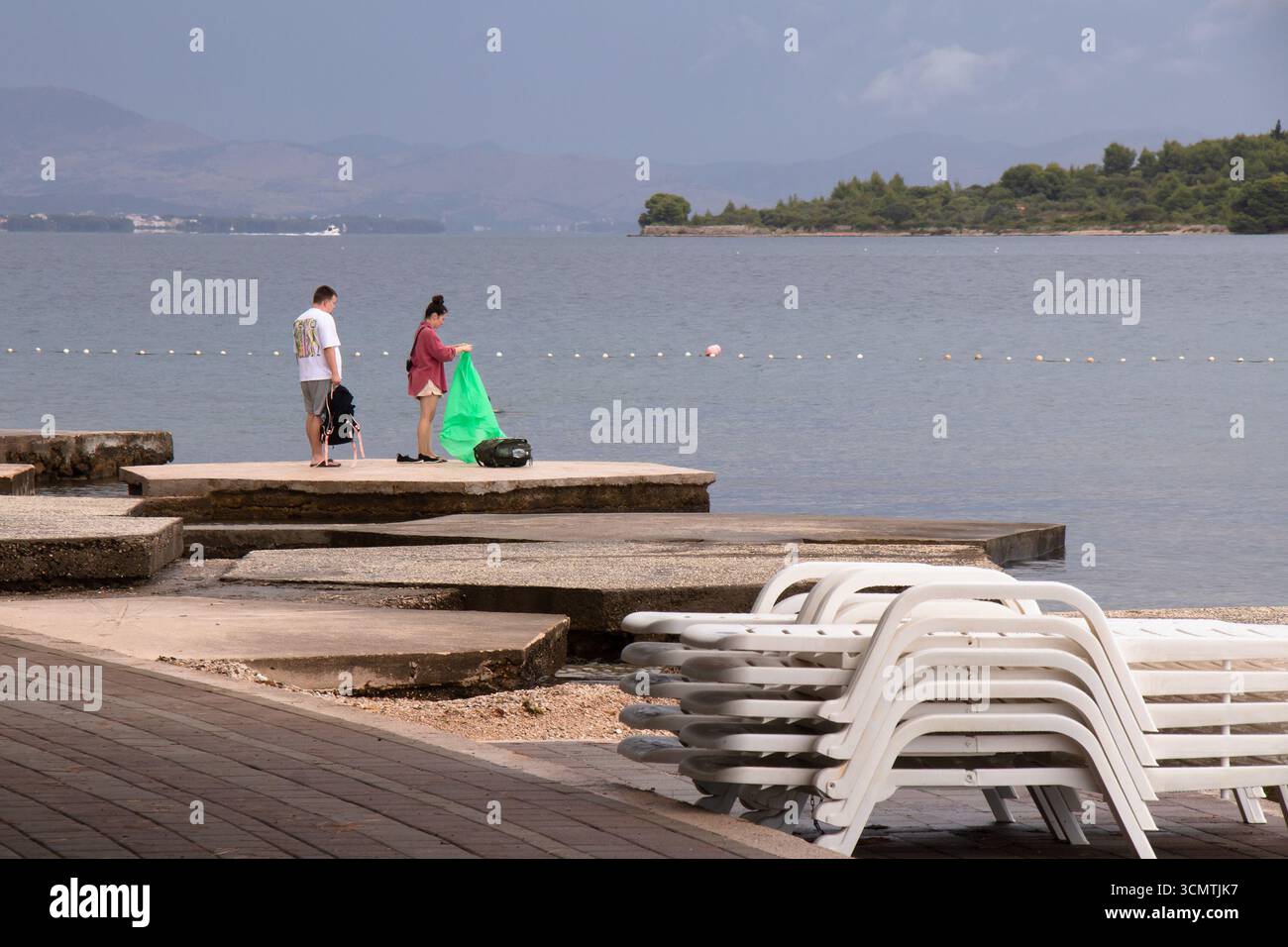 Vodice, Croazia - 30 agosto 2025: Lettini e giovani coppie che arrivano su una spiaggia vuota in una giornata estiva con tempo variabile su una costa Foto Stock