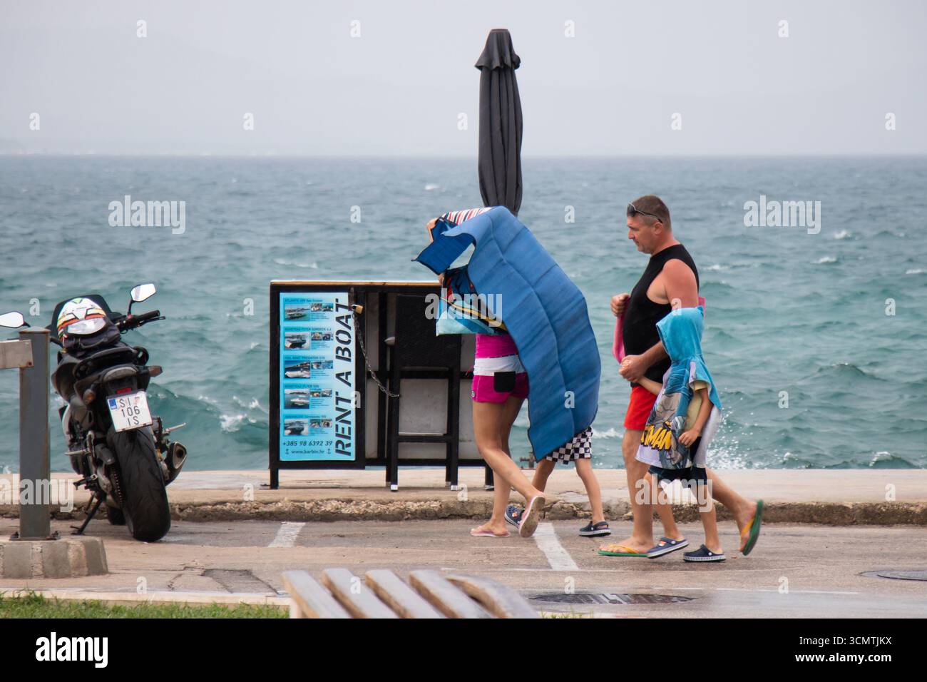 Vodice, Croazia - 21 agosto 2025: Famiglia di ritorno dalla spiaggia, in una giornata estiva piovosa sulla costa croata Foto Stock