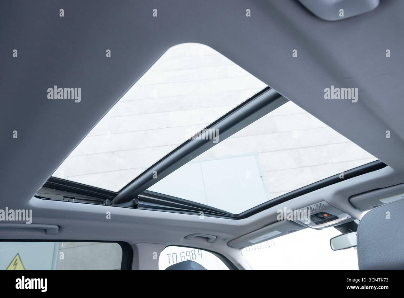 Interni SUV o wagon con rivestimento padiglione grigio chiaro e tetto panoramico. POV: Guardando verso l'alto la sezione del tetto in vetro dal sedile del passeggero posteriore. Foto Stock Interni SUV o wagon con rivestimento padiglione grigio chiaro e tetto panoramico. POV: Guardando verso l'alto la sezione del tetto in vetro dal sedile del passeggero posteriore. Foto Stock