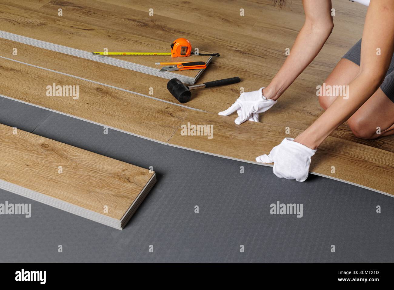 Vista ravvicinata dell'installatore femmina che monta tavole in vinile SPC con blocco a scatto e attrezzi su sottostrato per l'aggiornamento domestico Foto Stock