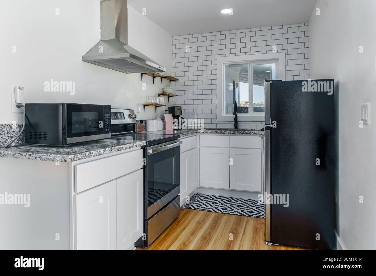 Piccola cucina bianca luminosa con elettrodomestici in acciaio inox e pareti in piastrelle della metropolitana Foto Stock