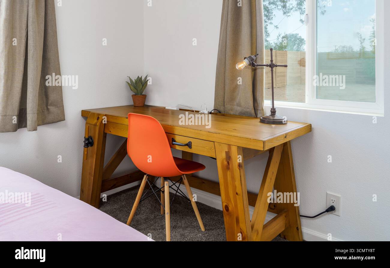 Scrivania in legno in una camera da letto con sedia arancione della metà del secolo e lampada, accanto alla finestra Foto Stock
