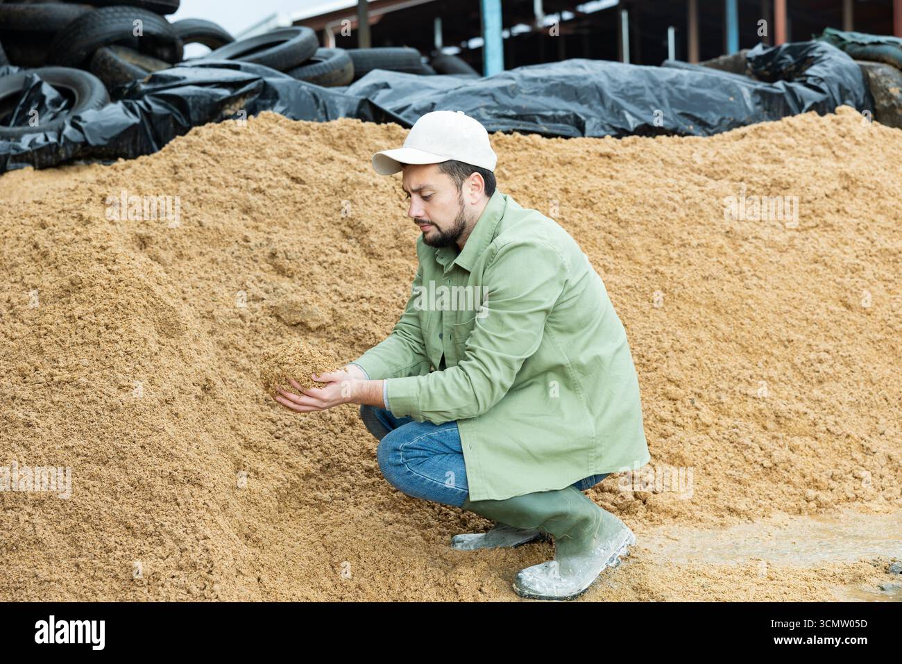 Coltivatore che squatting a mucchio grande di grano speso del birraio Foto Stock