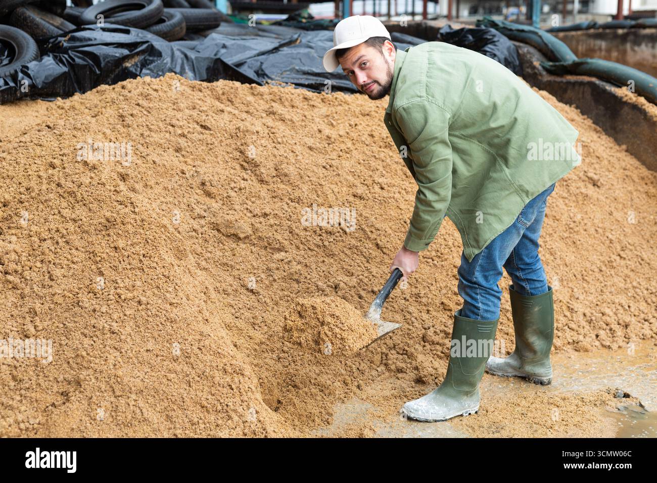 Agricoltore che spalanca un mucchio di bagasse di birra in un'area di stoccaggio aperta Foto Stock