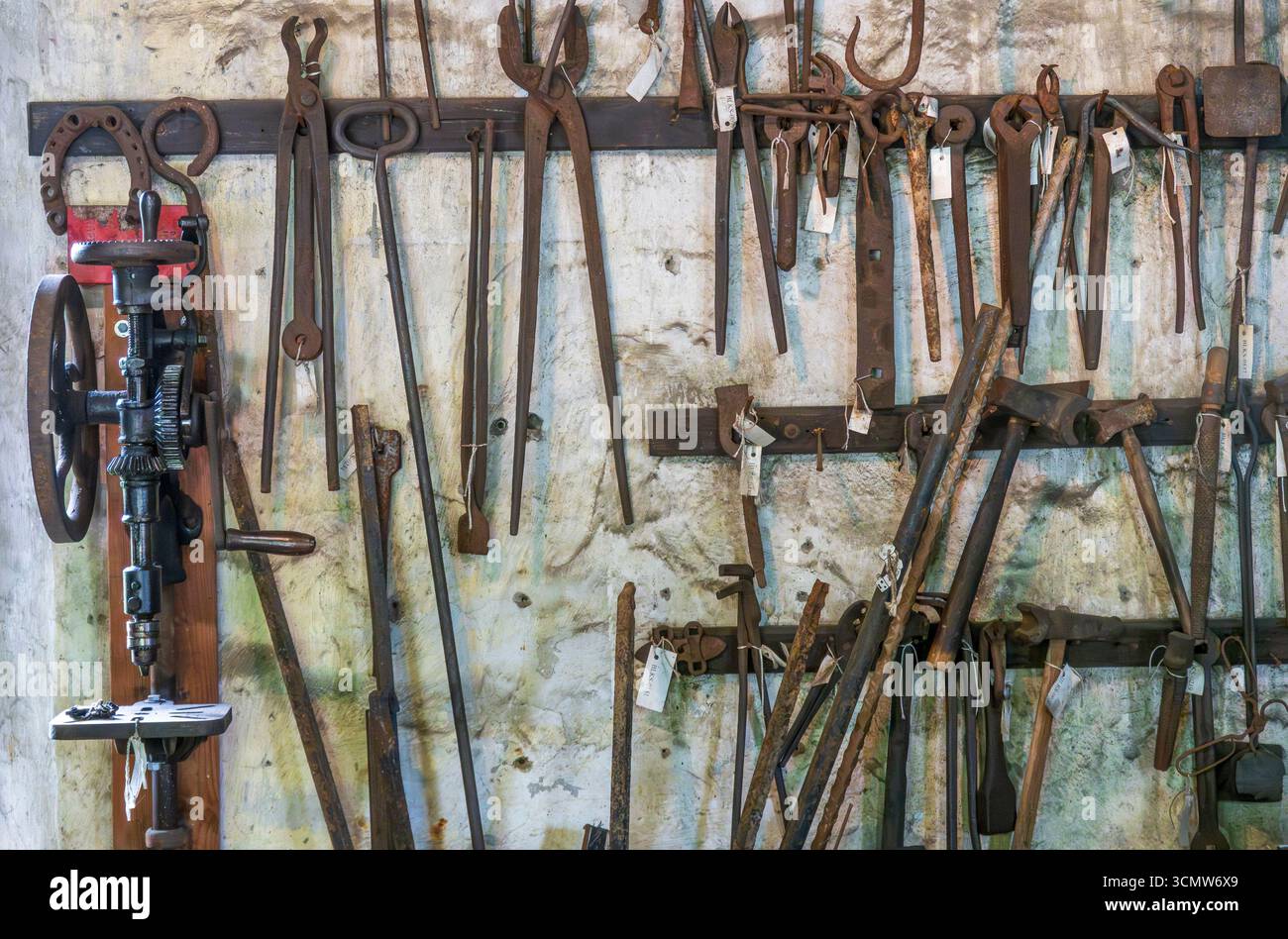 Monroe, New York - Stati Uniti - 6 settembre 2025 muro di utensili da fabbro vintage, martelli, pinze e pressa all'interno del negozio di fabbri Museum Village. Foto Stock