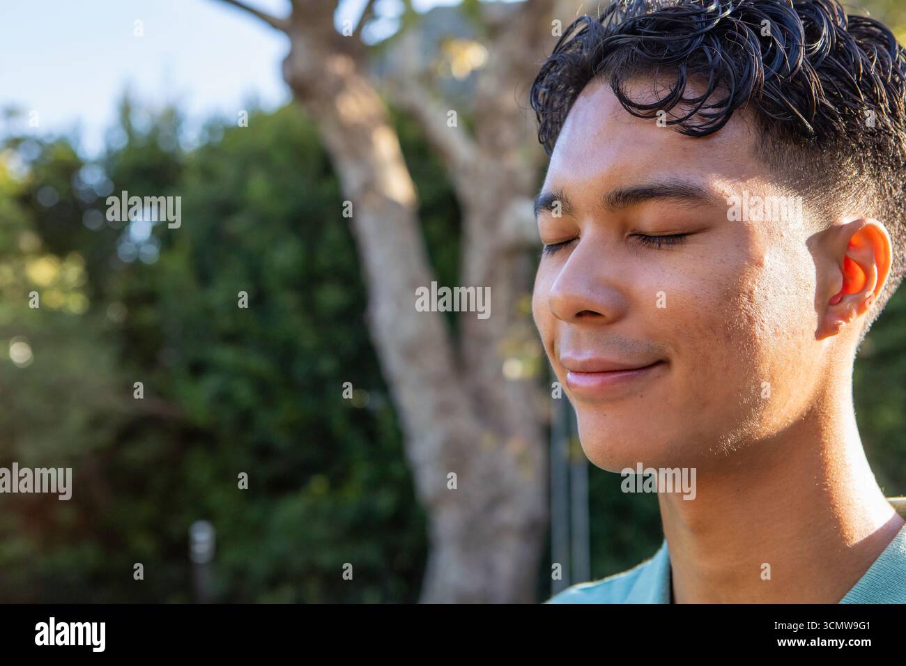 Uomo che indossa una camicia color verde acqua in piedi in giardino chiudendo gli occhi e sorridendo vicino agli arbusti, copiando spazio Foto Stock