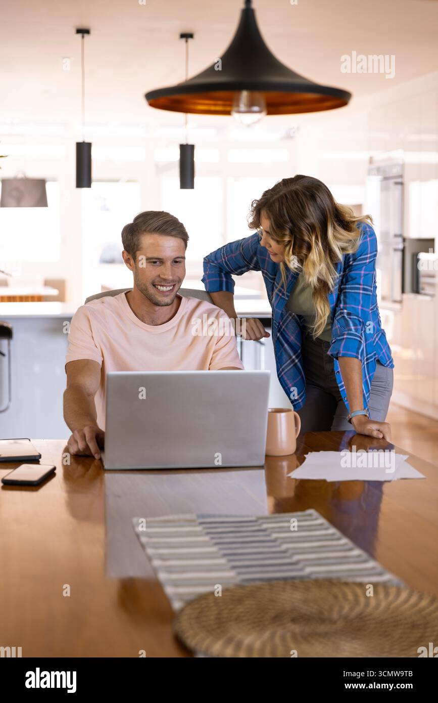 Coppia che lavora sul computer portatile al tavolo della cucina con carta per smartphone tazza da caffè Runner da tavolo a righe Foto Stock
