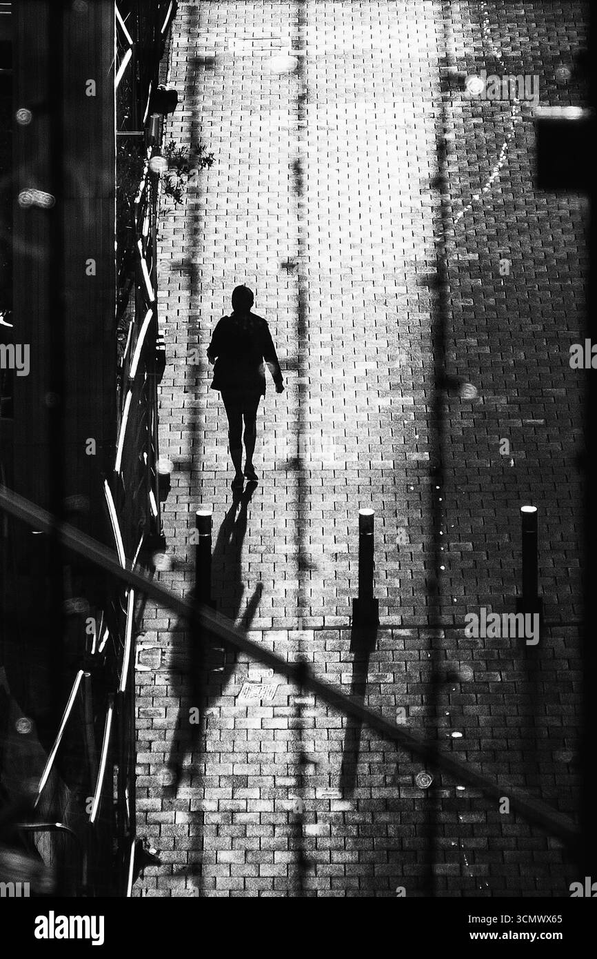 Persona che cammina su una strada acciottolata con una lunga ombra in bianco e nero Foto Stock
