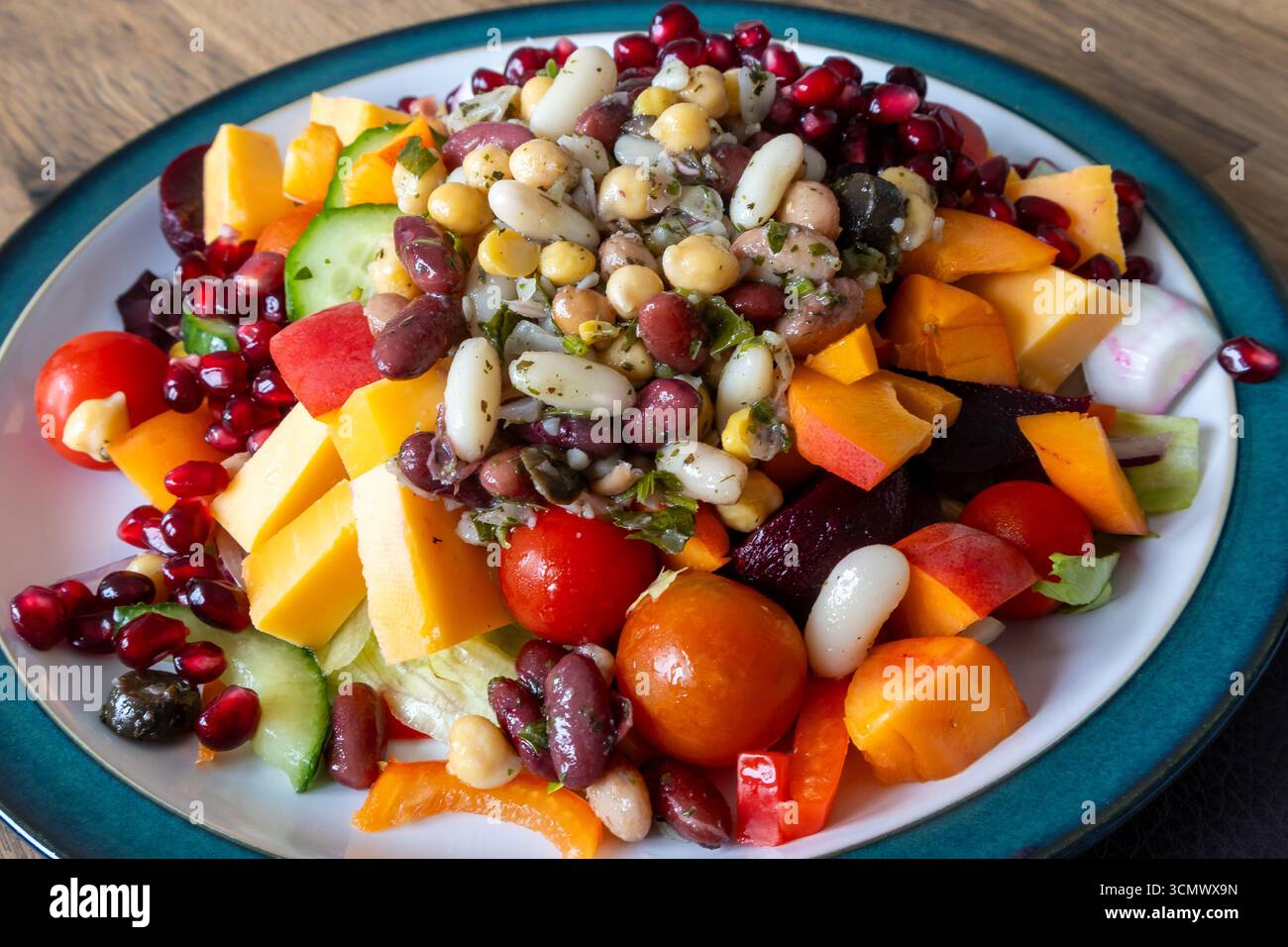 Piatto colorato di insalata con fagioli assortiti, pomodori ciliegini, cetrioli, peperoni, barbabietole, cubetti di formaggio e semi di melograno sul piatto Foto Stock