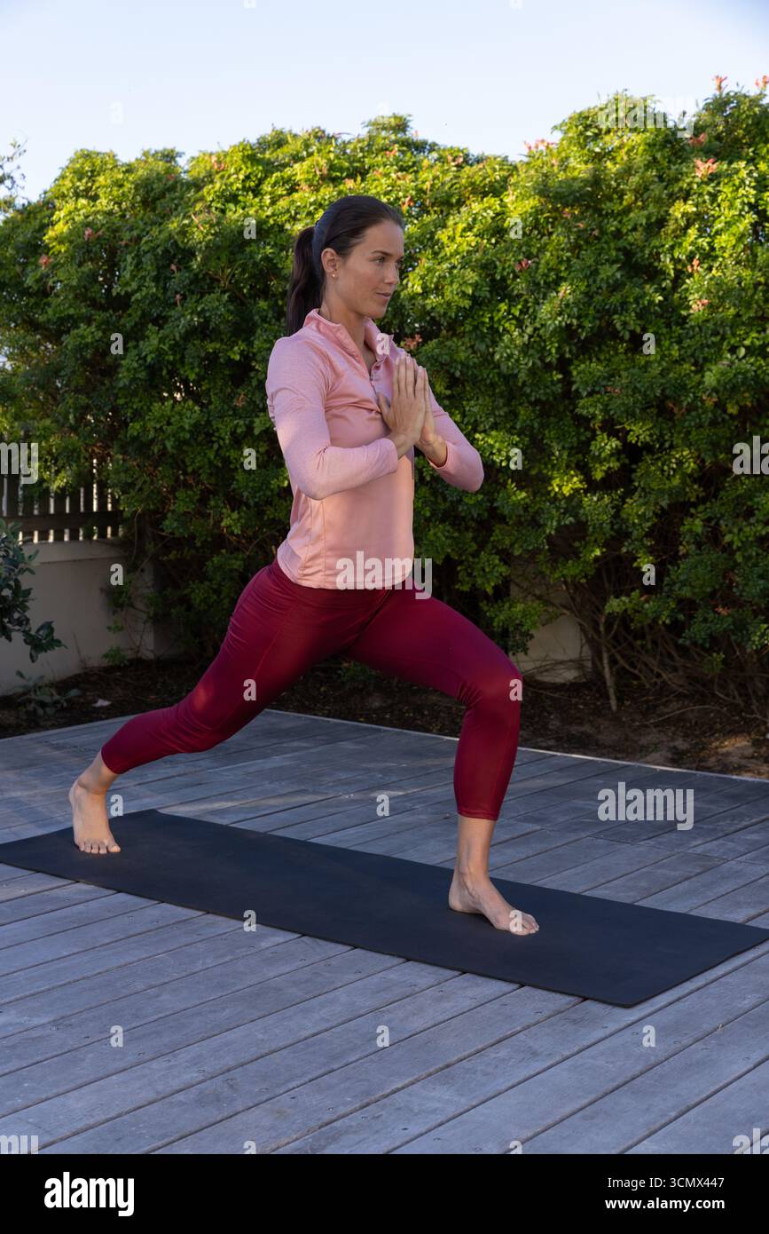 La posa dello yoga viene praticata sul tappetino sul ponte con arbusti verdi sotto la luce del sole mattutino Foto Stock